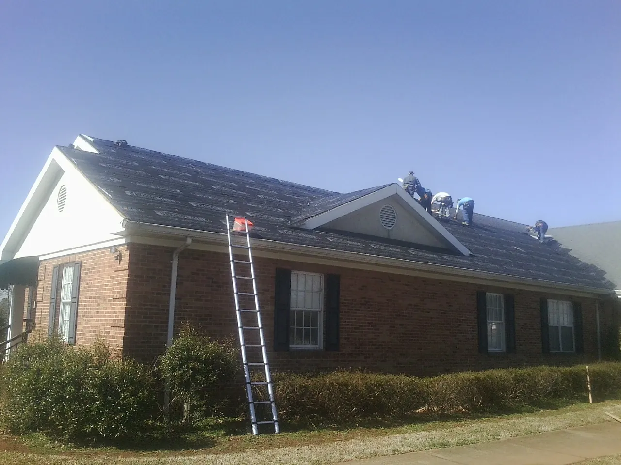 Crew tearing shingles off a brick ranch roof with a ladder set — Metal Roof Repair work by our crew in North Liberty