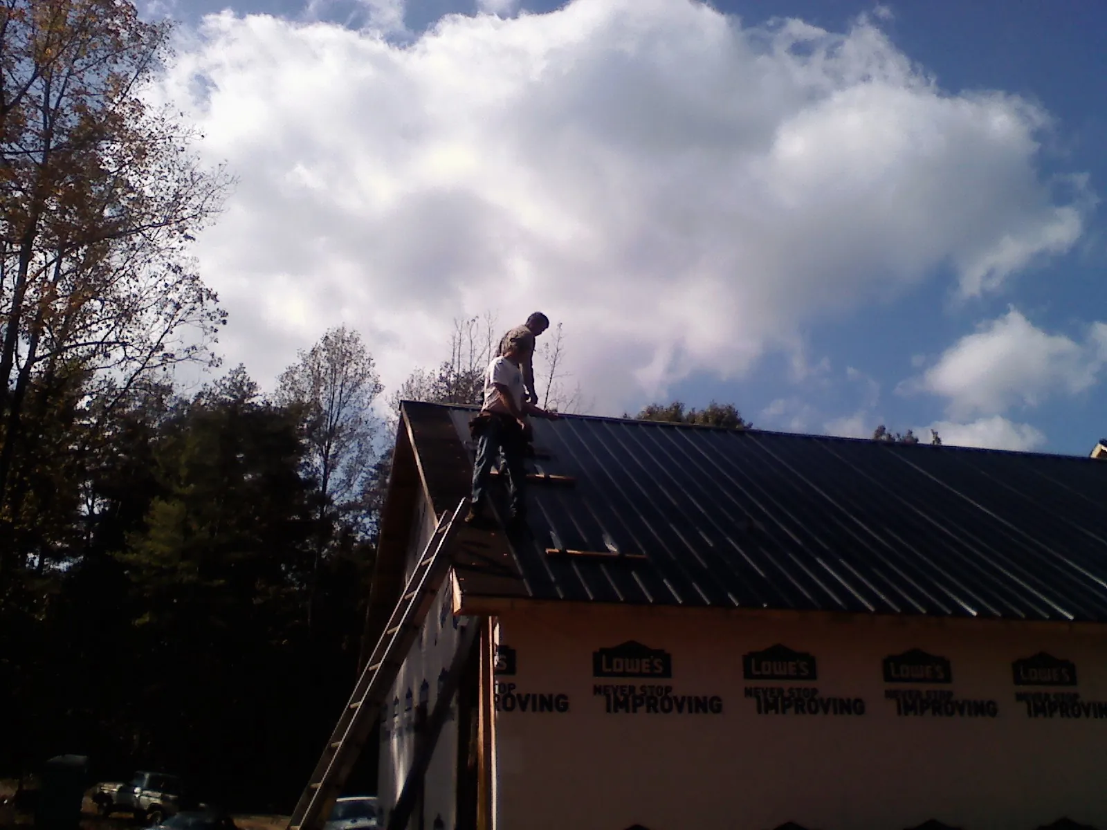 Roofer fastening dark metal panels high against a cloudy sky, from a Roof Inspection job in North Liberty