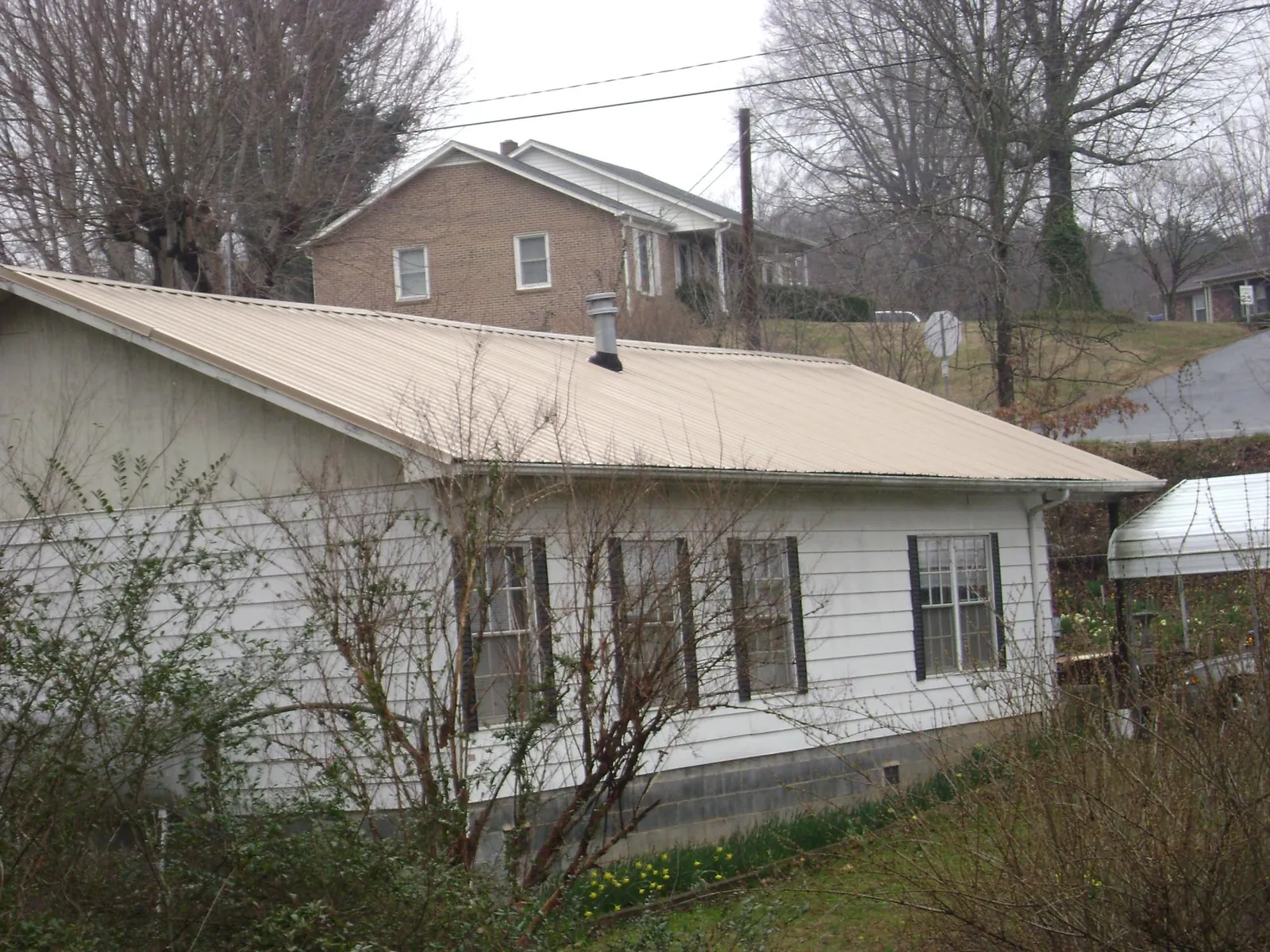 Tan metal roof on a white sided house set into a hillside — Commercial Roofing by Roofing Brothers in North Liberty