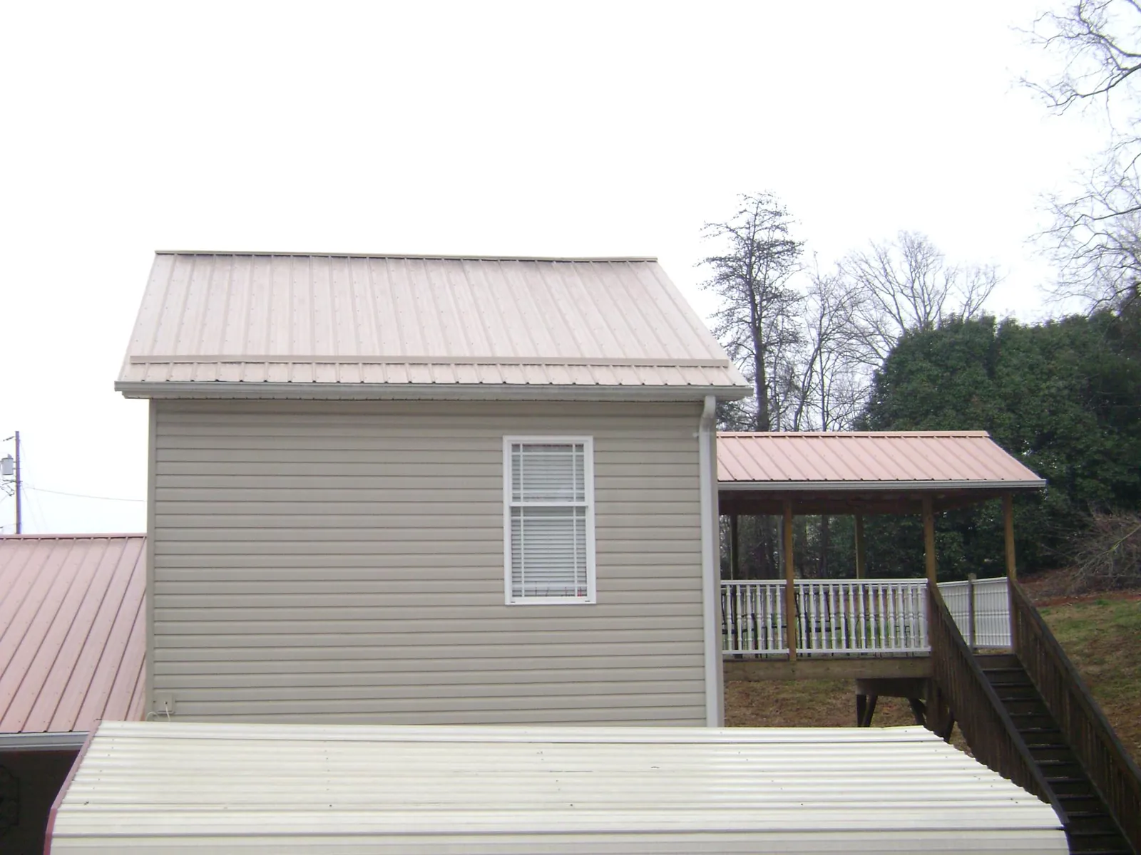 Tan metal roofs on a two story addition and attached porch, from a Roof Replacement job in North Liberty