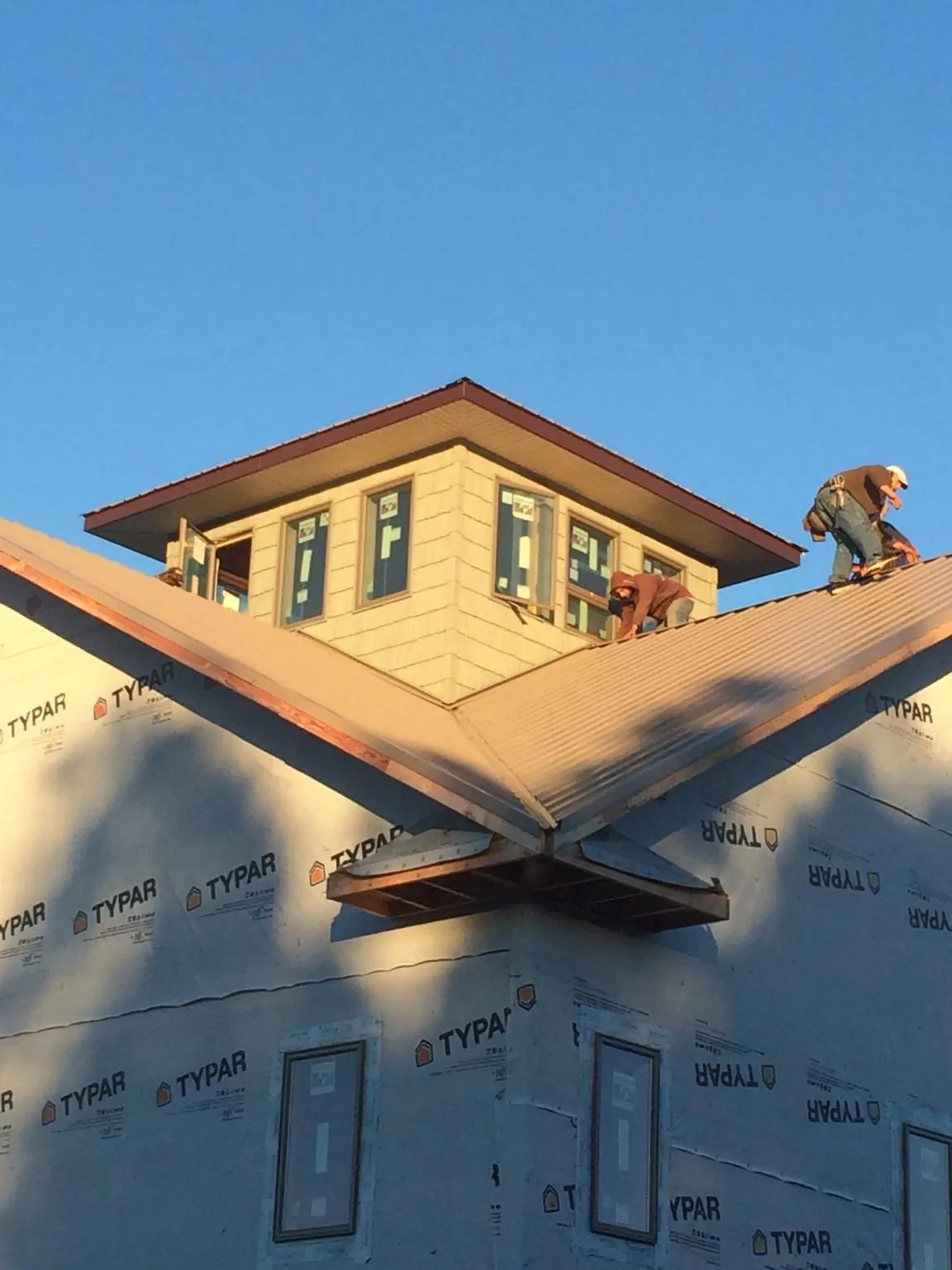 Roofers working around a rooftop cupola on a new metal roof at sunset — Roof Waterproofing in North Liberty by Roofing Brothers